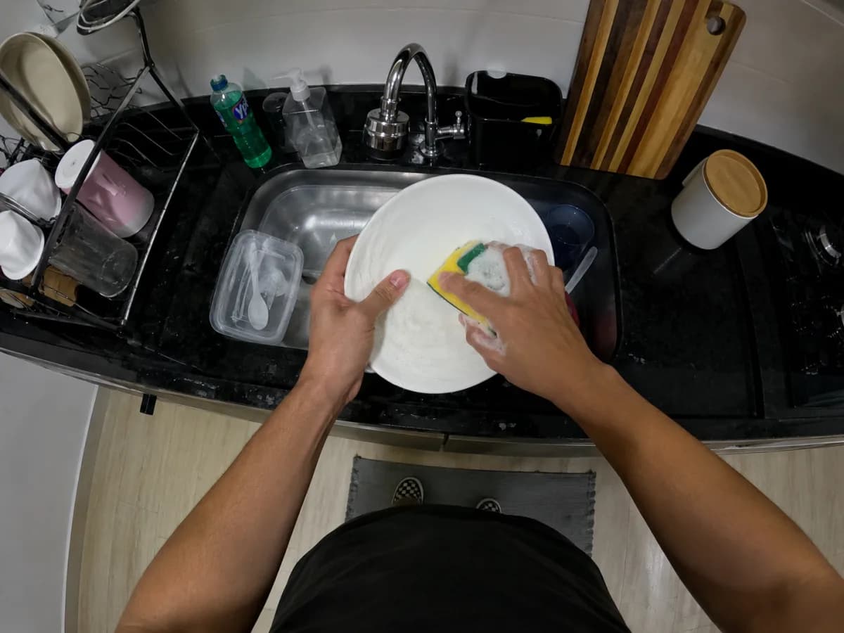 Pessoa lavando louça com as mãos e a tarefa inteiramente visíveis